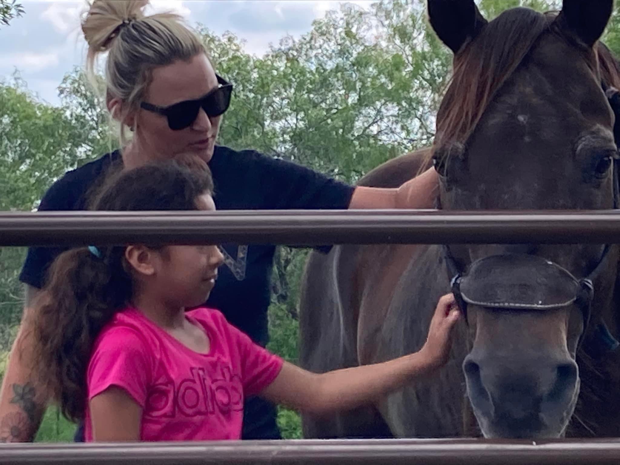 a child pets a horse with the assistance of a staff member